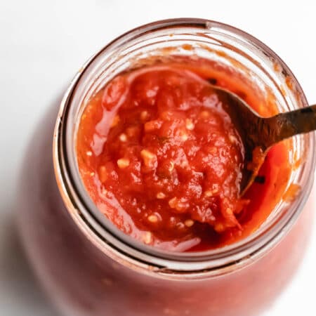 A spoon scooping pizza sauce from a glass jar.