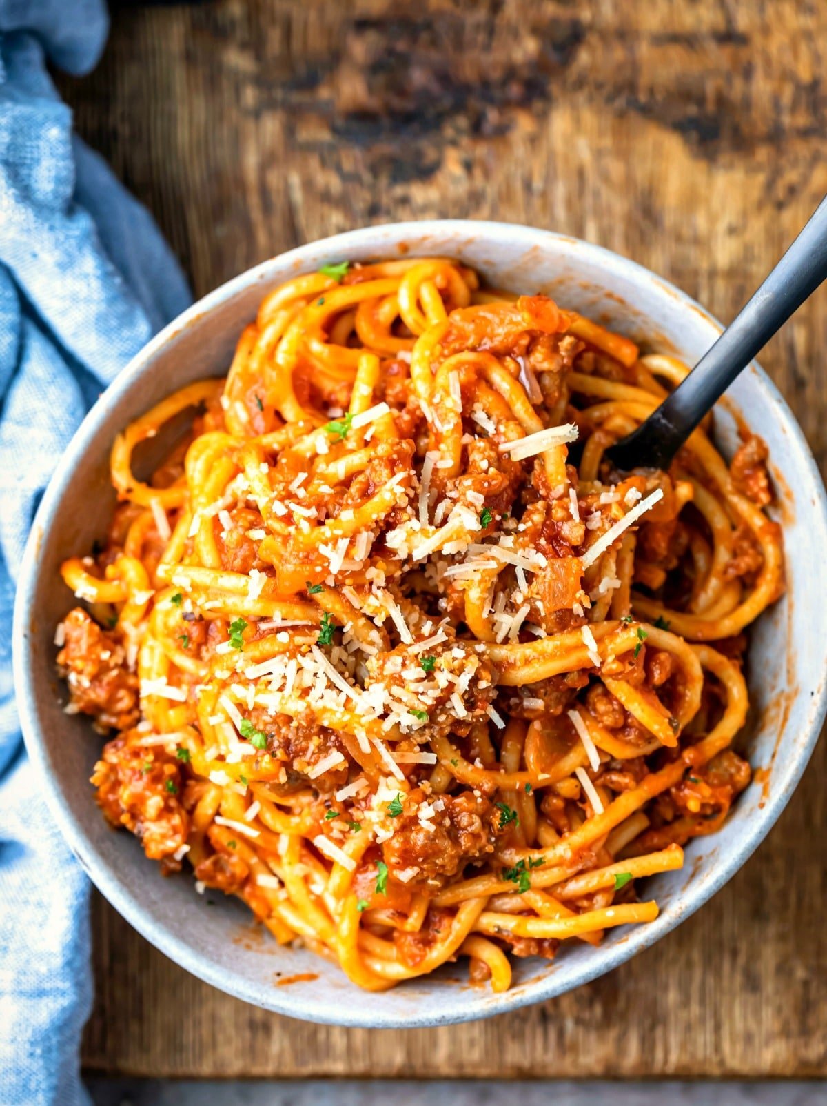 Blue bowl with spaghetti and meat sauce on a wooden cutting board.