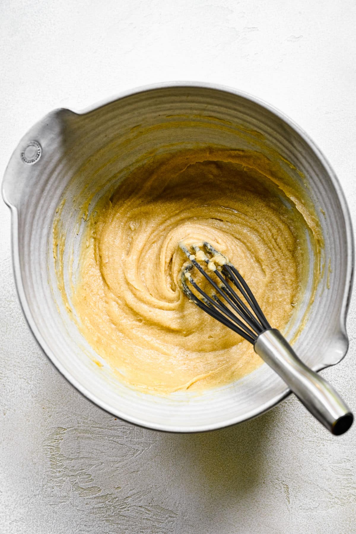 A whisk in butter sugar mixture in a mixing bowl. 
