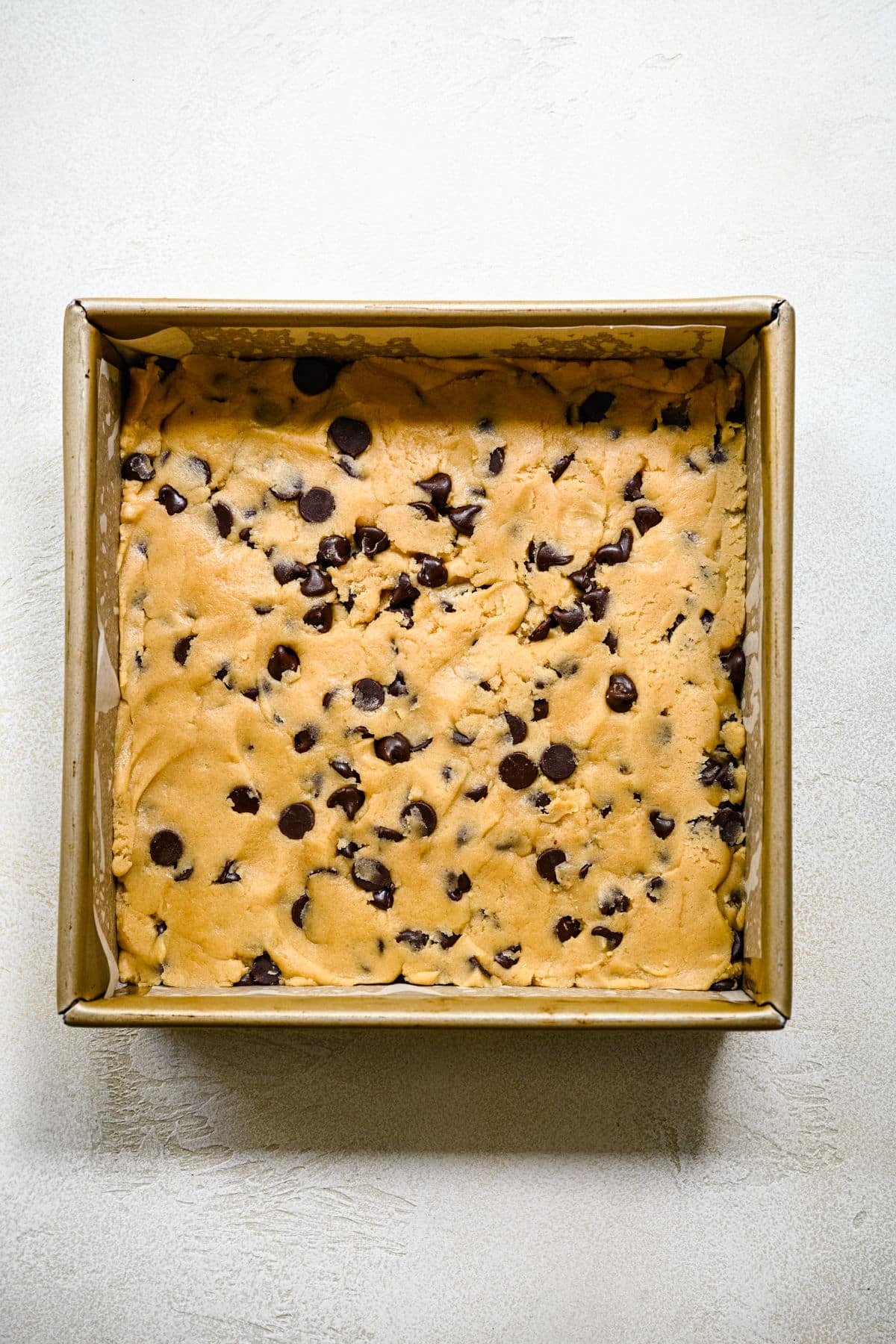 Chocolate chip cookie bar dough in a square baking pan.