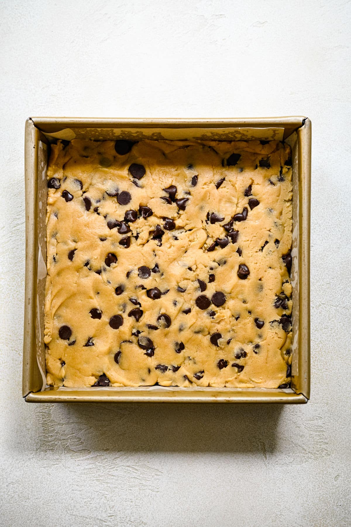 Chewy Chocolate Chip Cookie Bar Recipe Chocolate chip cookie bar dough in a square baking pan.