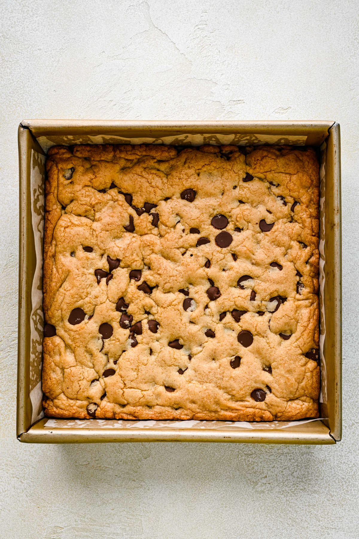 Baked chocolate chip cookie bars in a square baking pan.