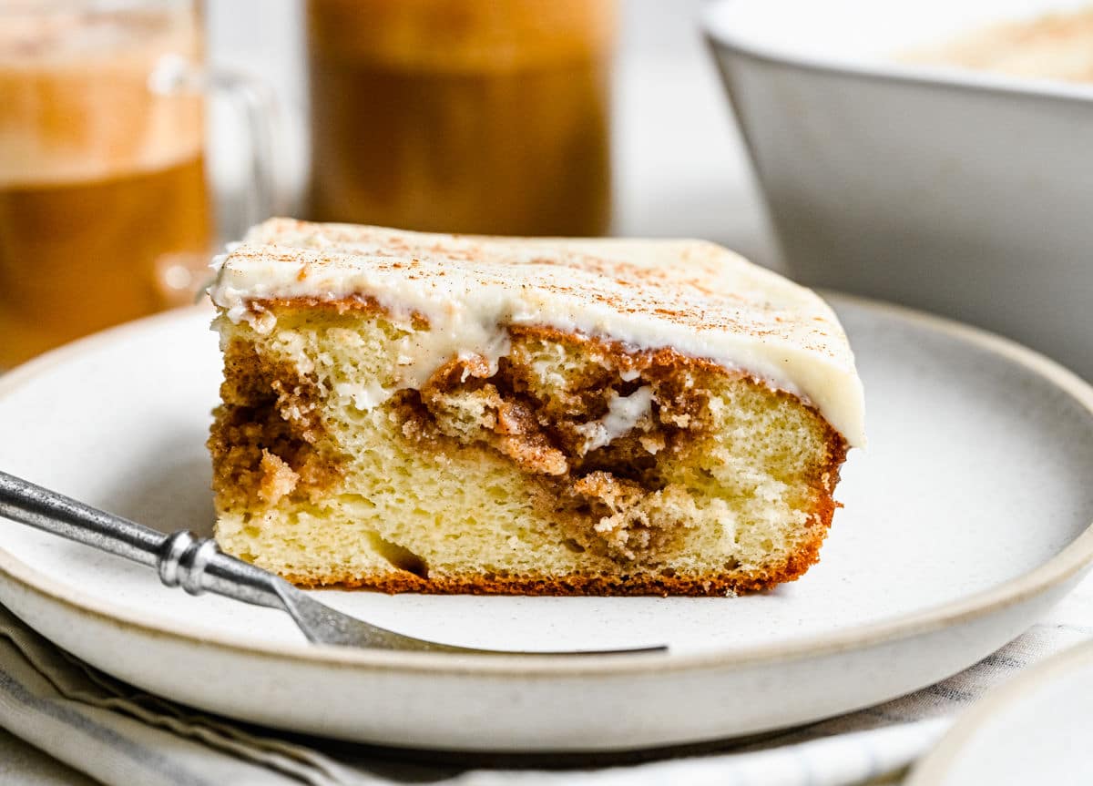 A slice of cinnamon roll poke cake on a plate with a fork.