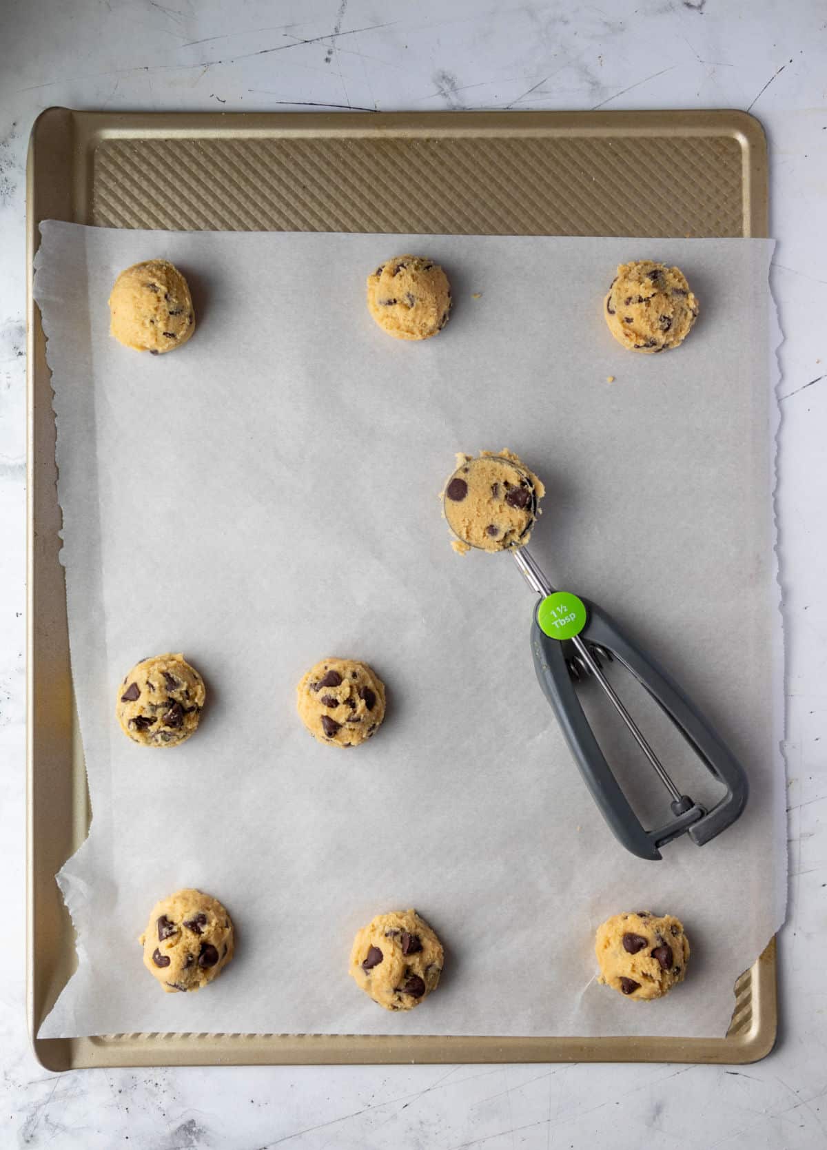 A cookie scoop full of cookie dough on a baking sheet. 