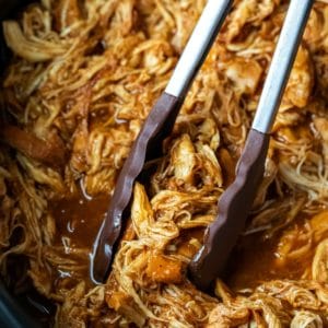 Tongs grabbing crock pot brown sugar bourbon bbq chicken in a crock pot