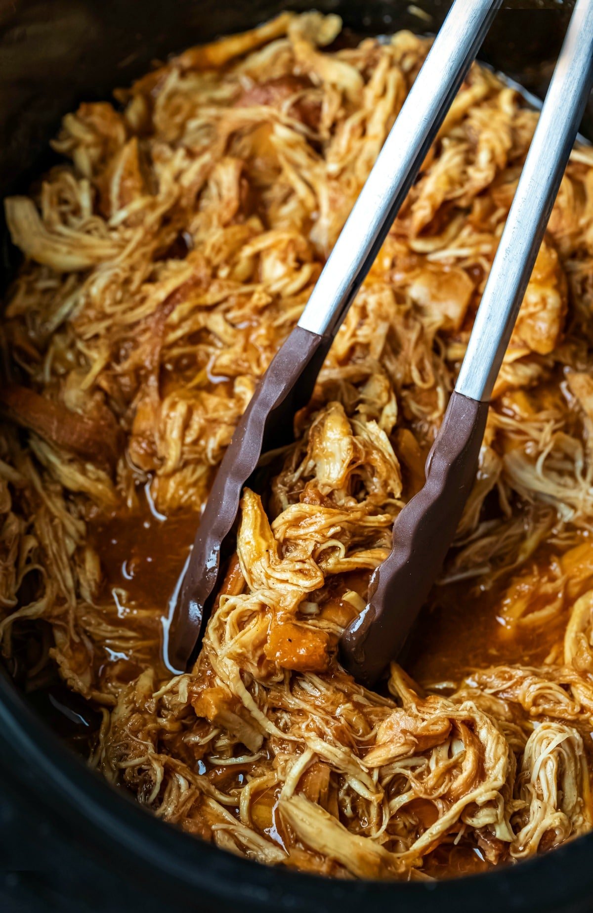 Tongs grabbing crock pot brown sugar bourbon bbq chicken in a crock pot