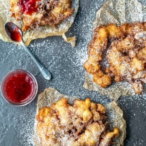 Three homemade funnel cakes on pieces of brown parchment paper