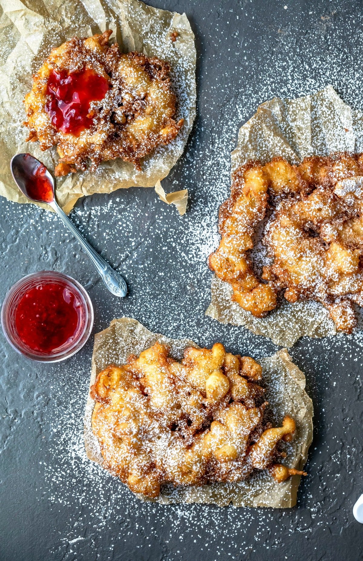 Three homemade funnel cakes on pieces of brown parchment paper.