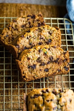 Three slices of chocolate chip zucchini bread on a gold wire cooling rack