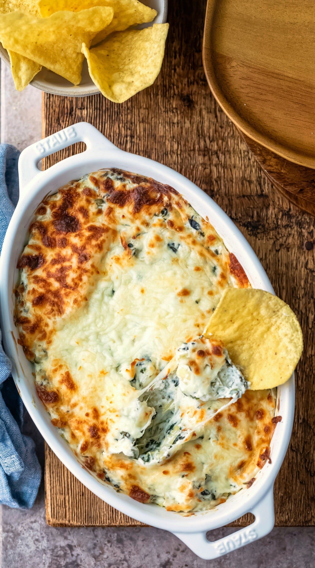 White dish of spinach artichoke dip next to a bowl of tortilla chips.