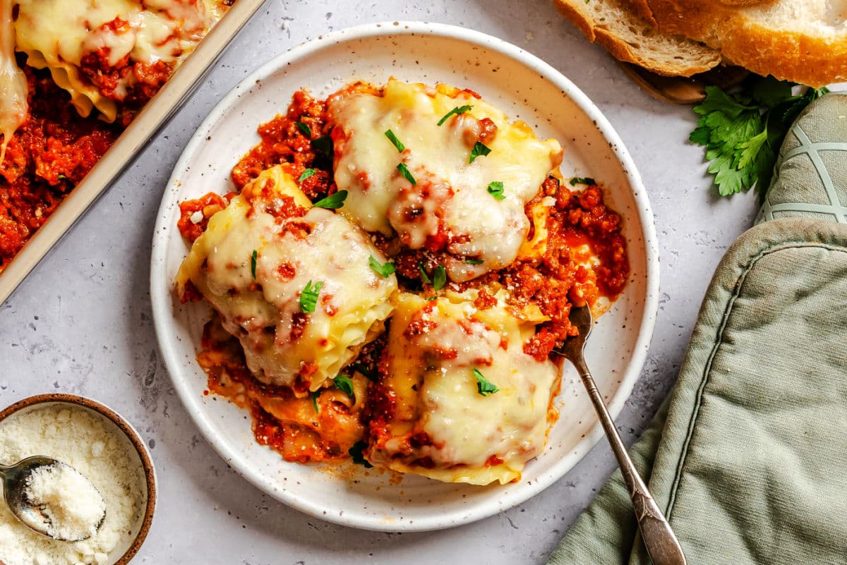 A plate with 3 lasagna rolls on it next to slices of bread. 