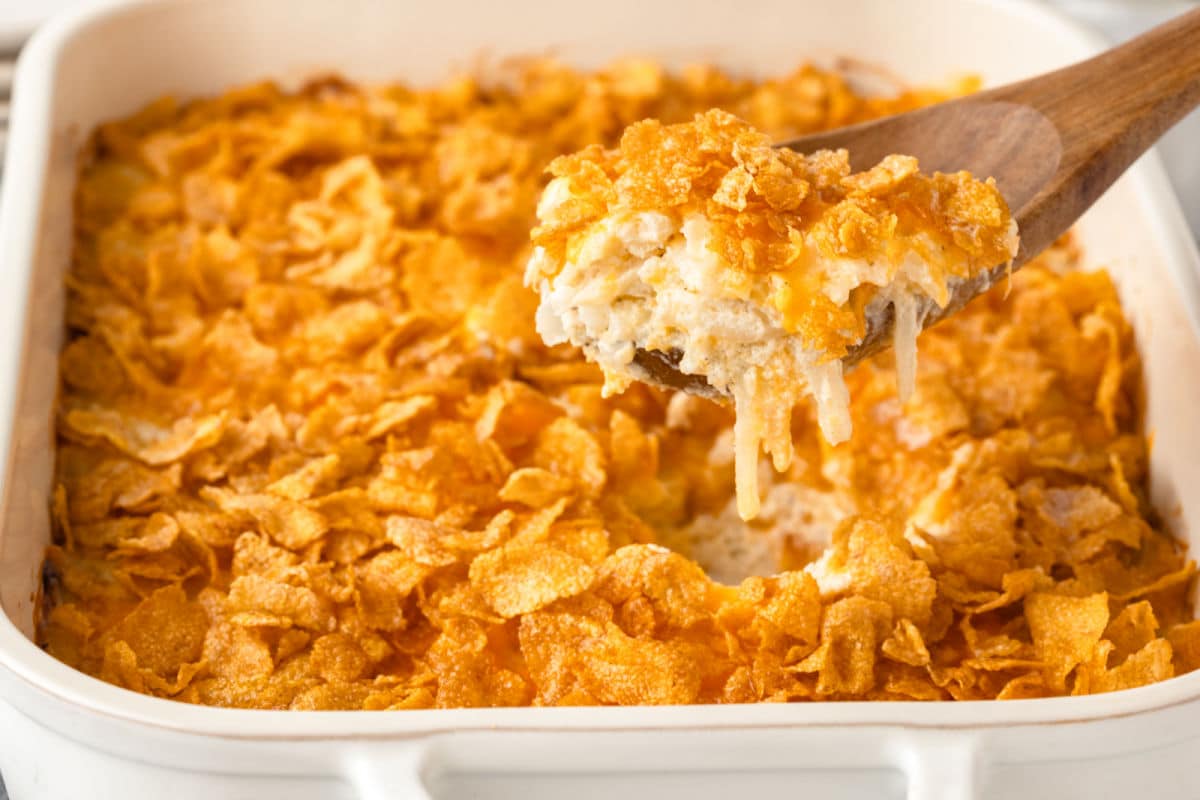A wooden spoon scooping up some funeral potatoes from a pan.