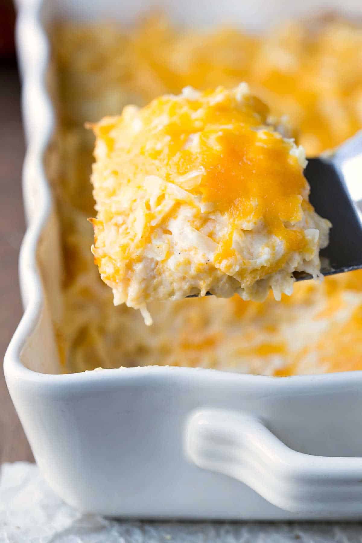 A scoop of funeral potatoes coming up out of a pan.