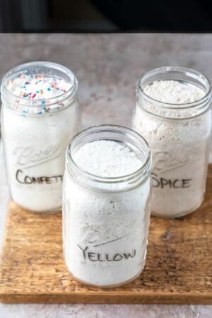 Three jars of homemade cake mix on a wooden cutting board.
