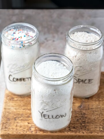 Three jars of homemade cake mix on a wooden cutting board.