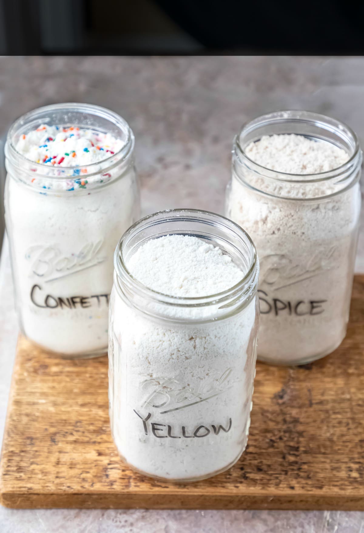 Three jars of homemade cake mix on a wooden cutting board.