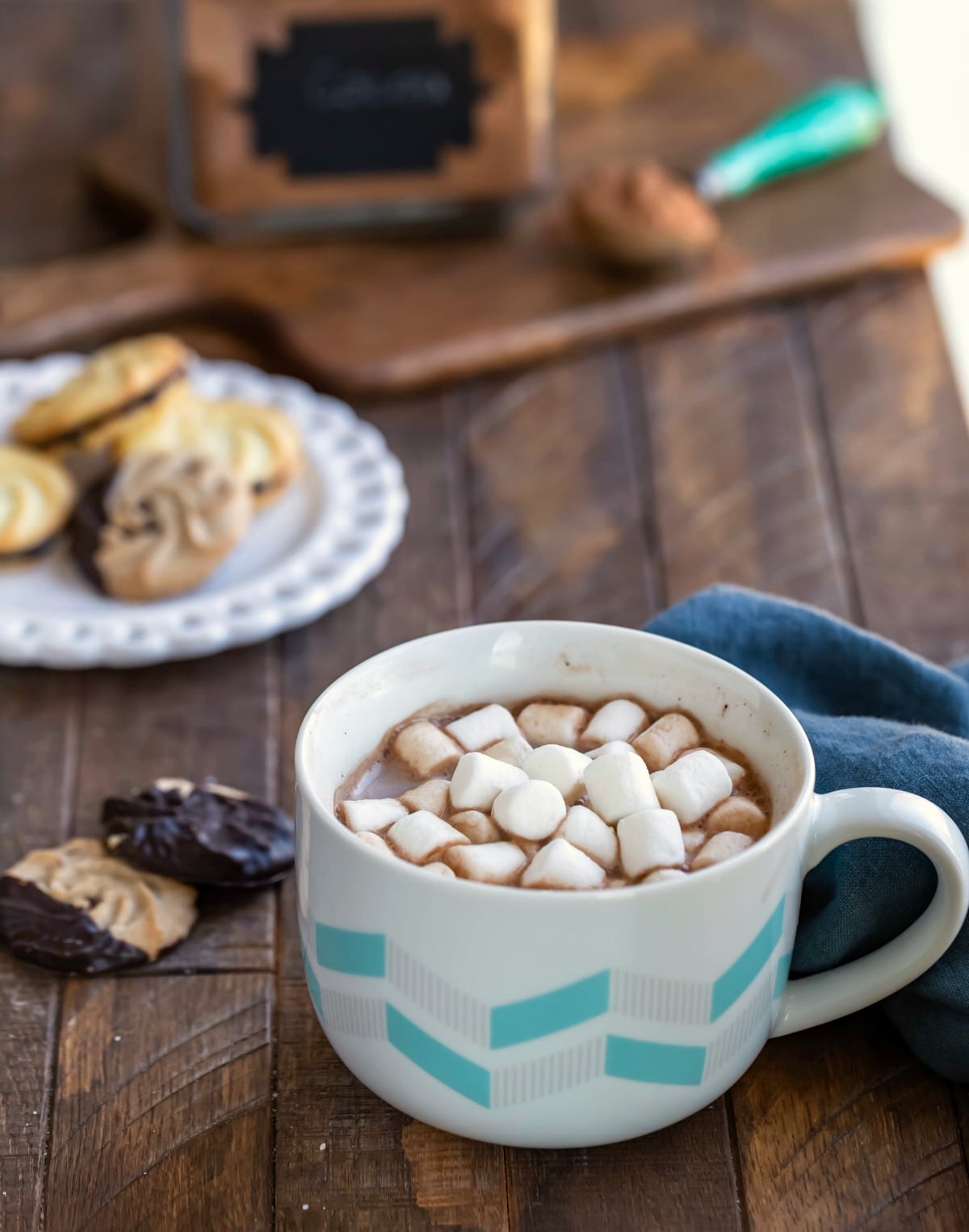 Mug of hot cocoa next to a plate of cookies