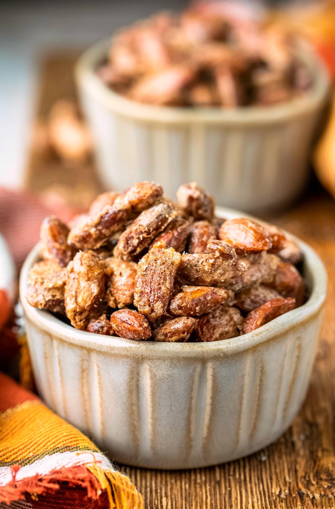 Two ramekins of cinnamon almonds on a wooden cutting board