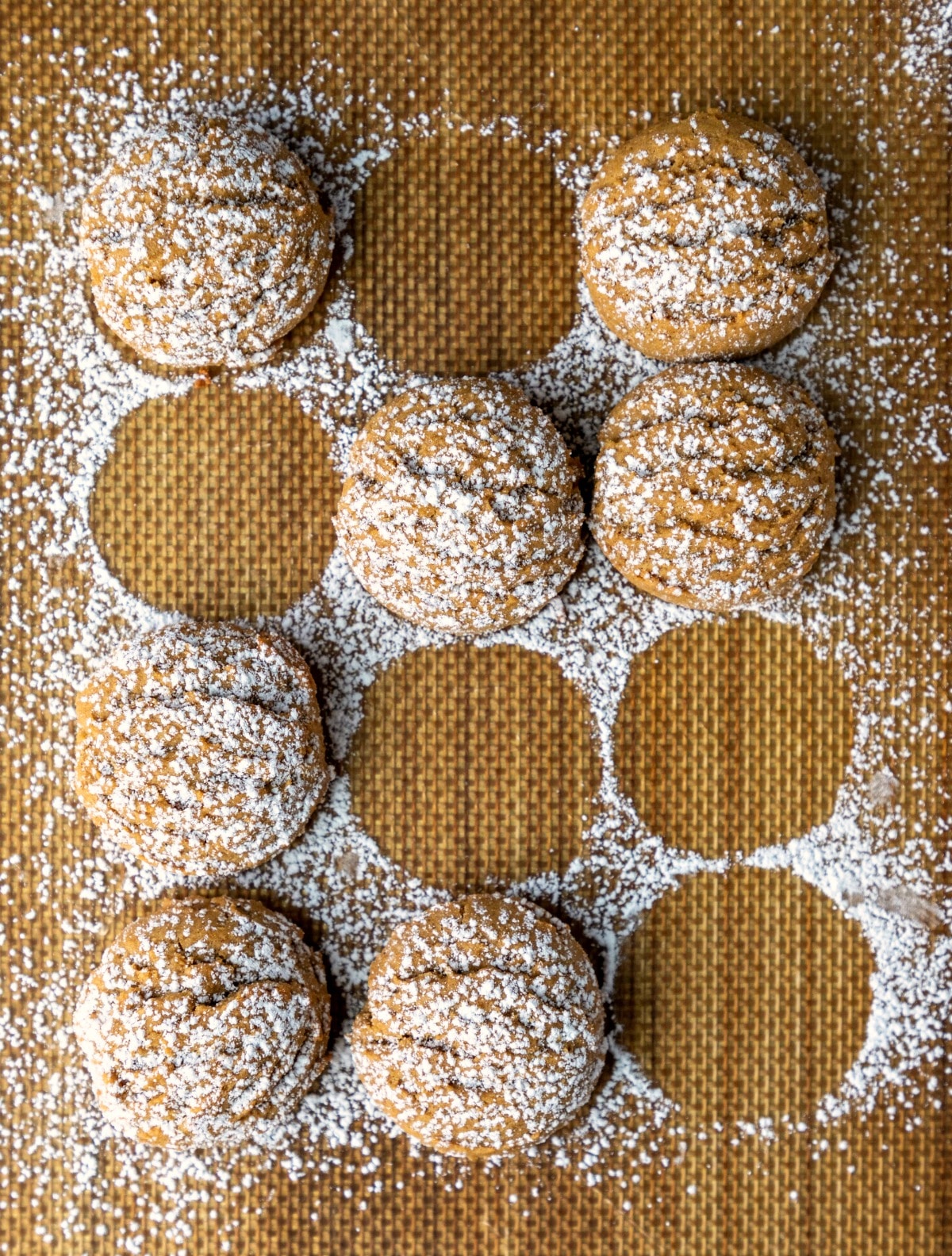 Pfeffernusse cookies sprinkled with powdered sugar on a baking mat