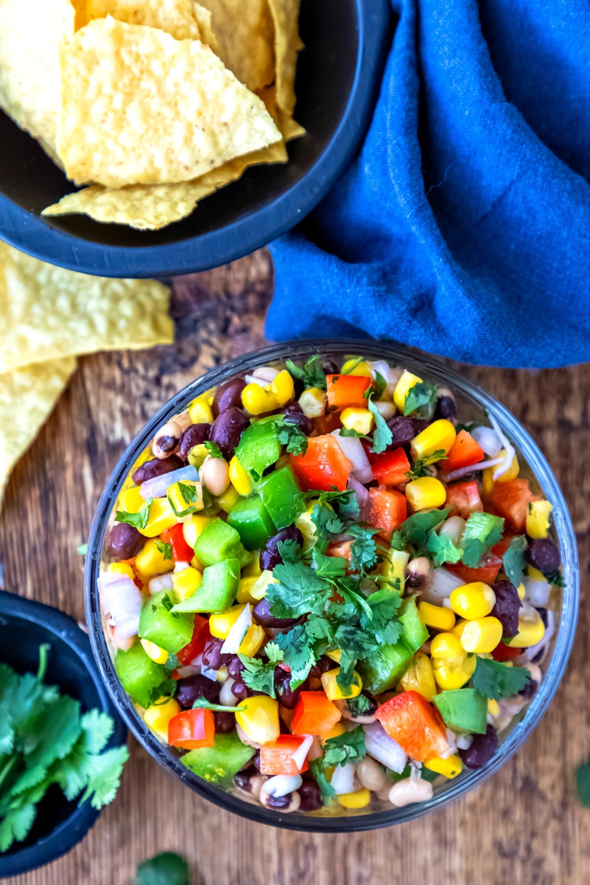 glass dish with cowboy caviar next to bowls of chips and cilantro