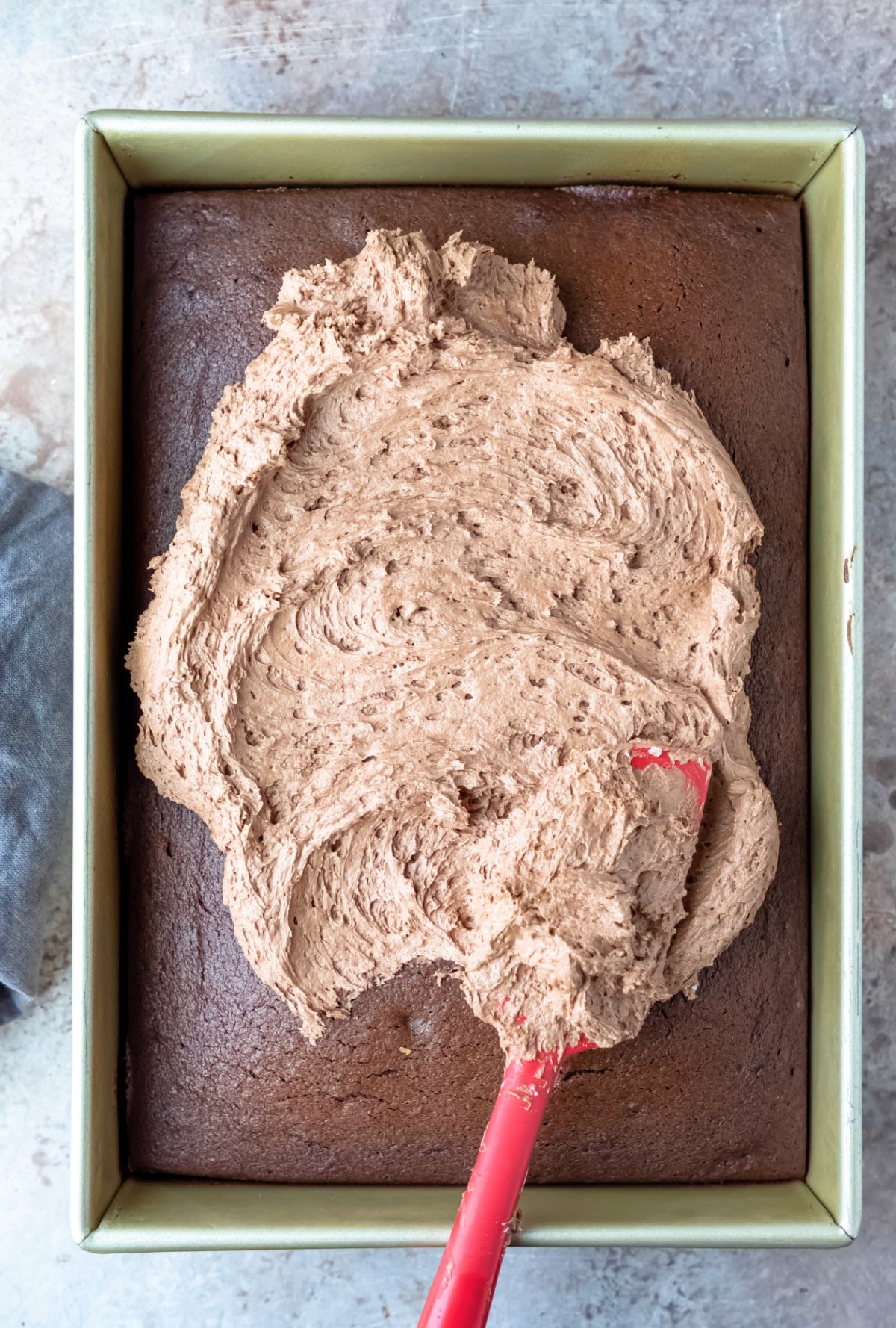 Red spatula spreading chocolate frosting on a cake