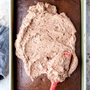 A spatula spreading melted chocolate buttercream on a chocolate cake