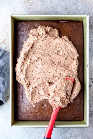 A spatula spreading melted chocolate buttercream on a chocolate cake