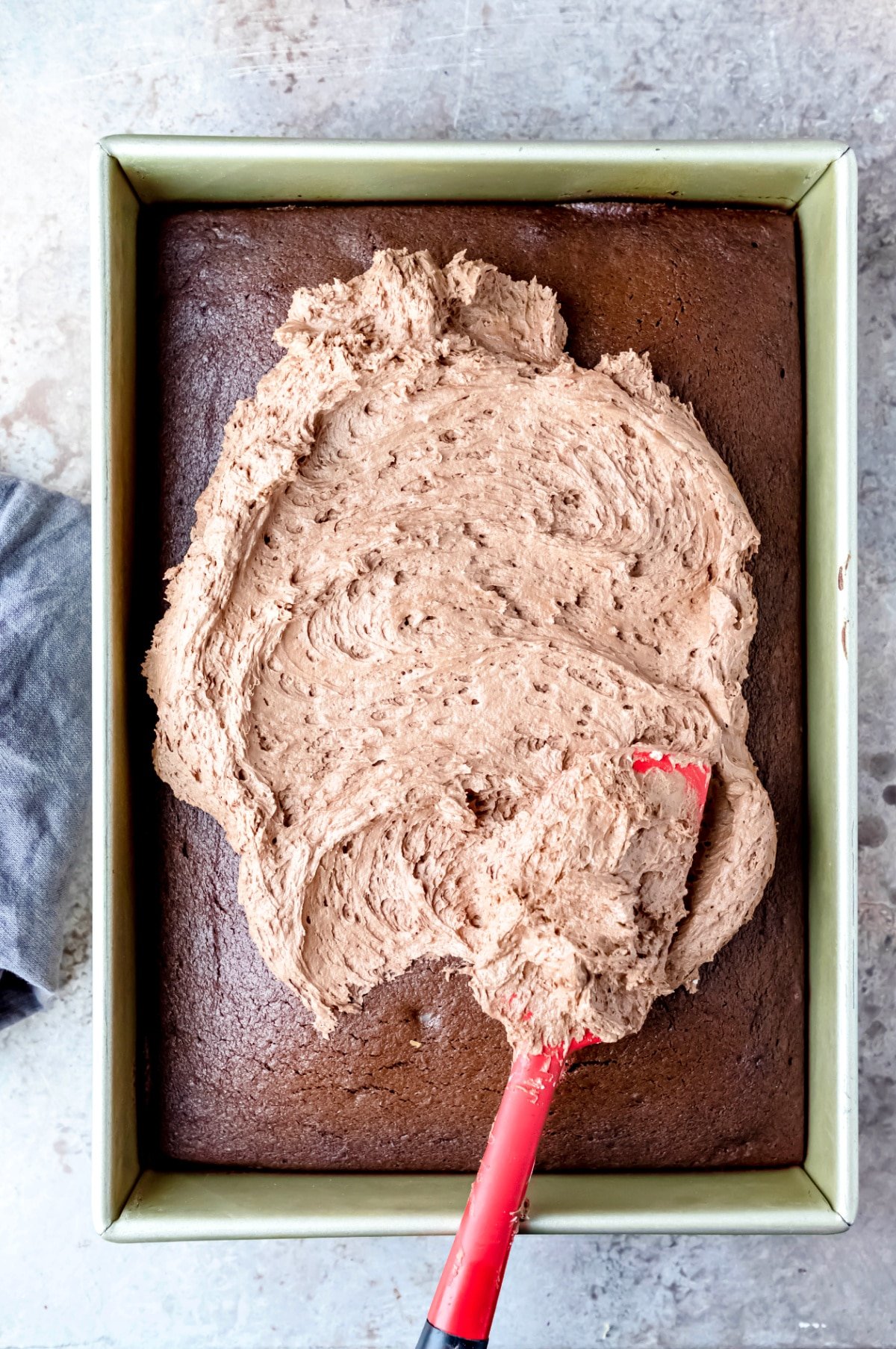 A spatula spreading melted chocolate buttercream on a chocolate cake