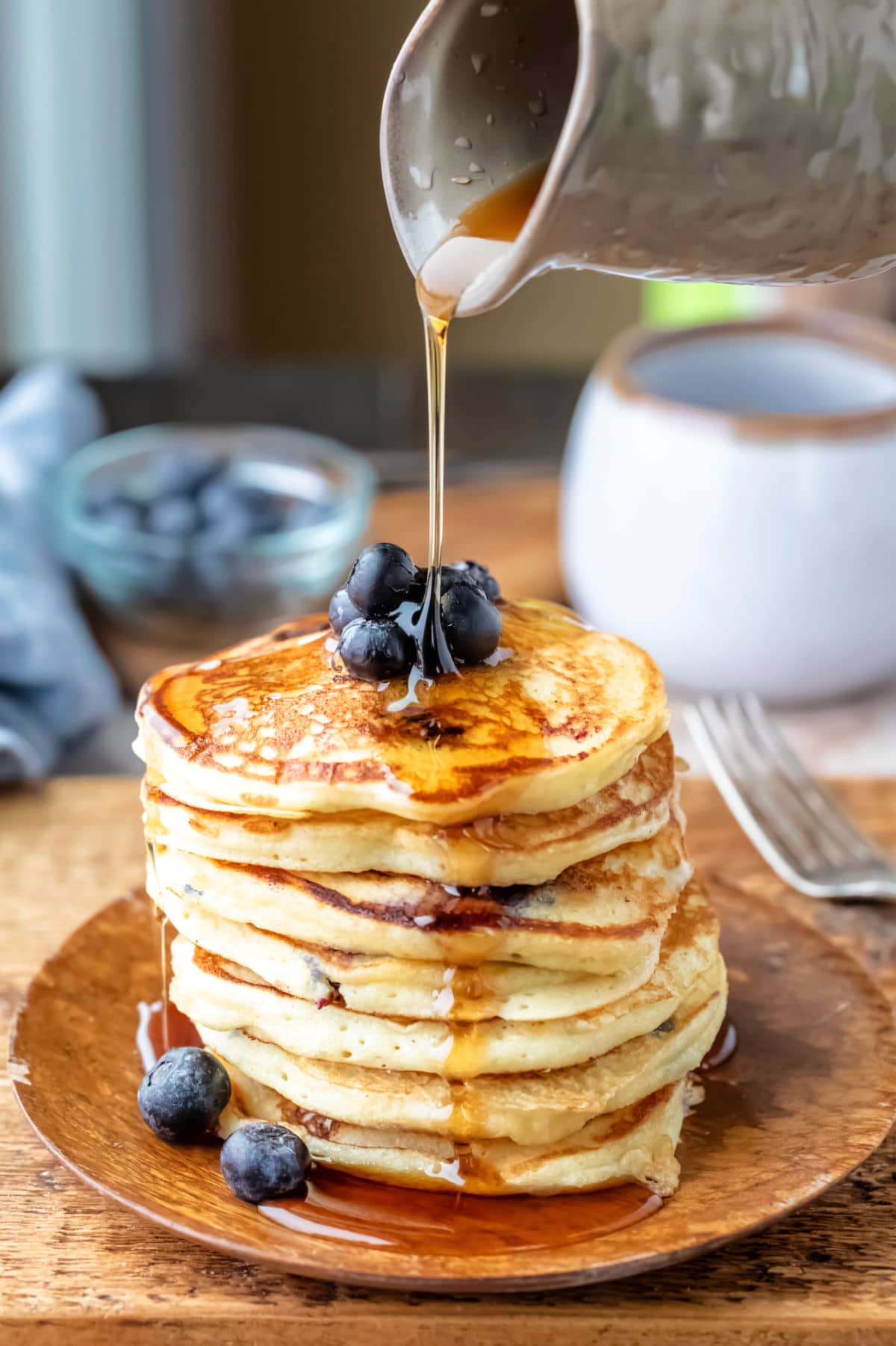 Maple syrup pouring onto a stack of blueberry lemon ricotta pancakes