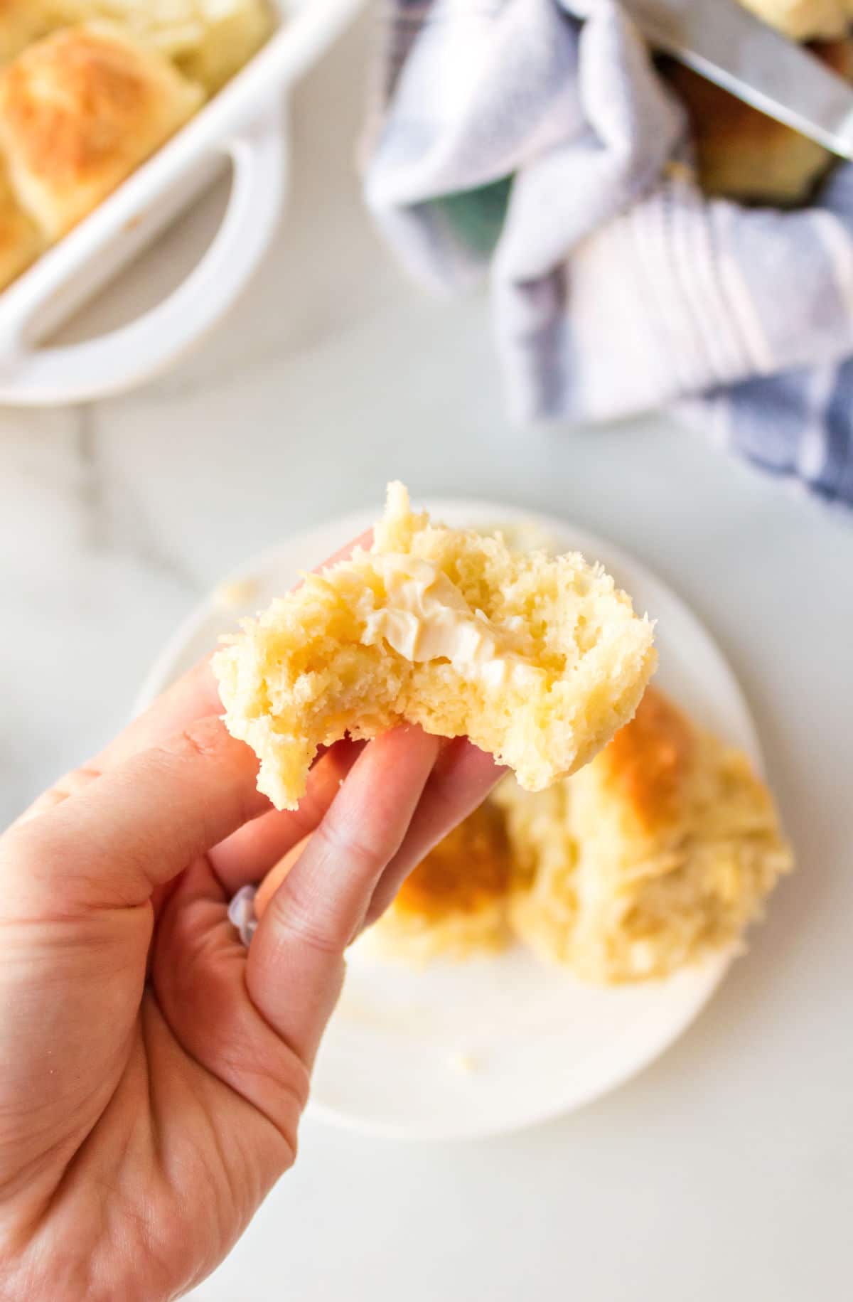 Hand holding part of a buttered Amish dinner roll.
