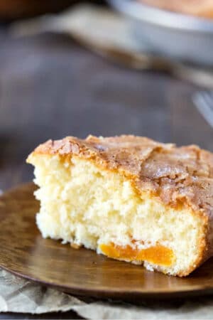 Slice of apricot cake on a wooden plate.