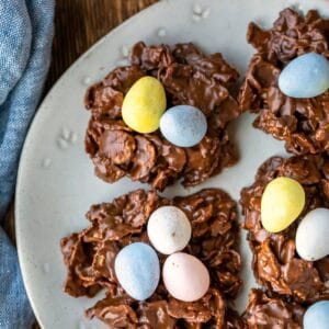 A plate of bird's nest cookies next to a dish of candy eggs.