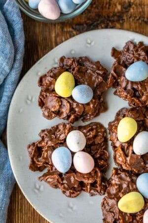 A plate of bird's nest cookies next to a dish of candy eggs.