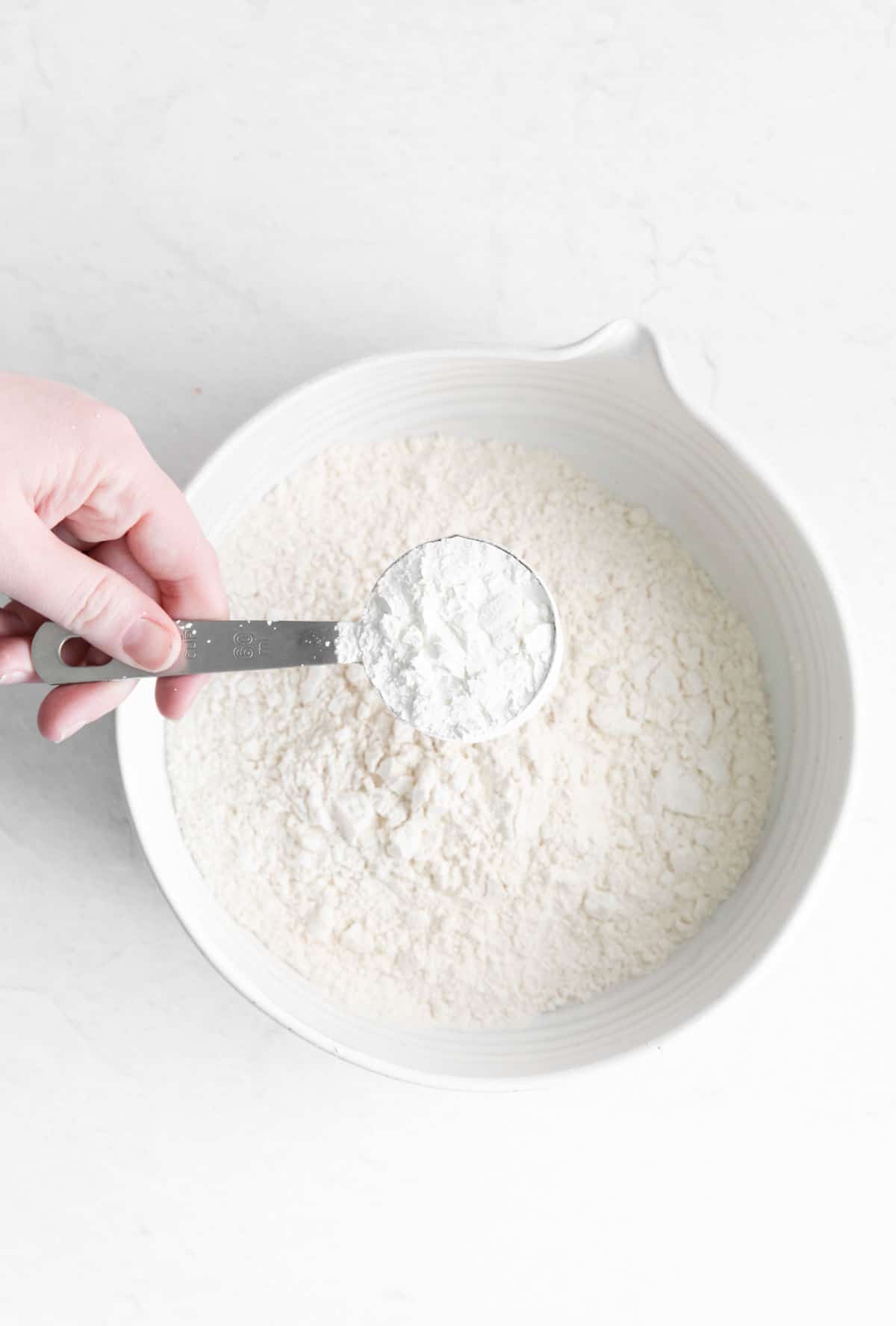 Measuring spoon removing flour from a bowl of flour.