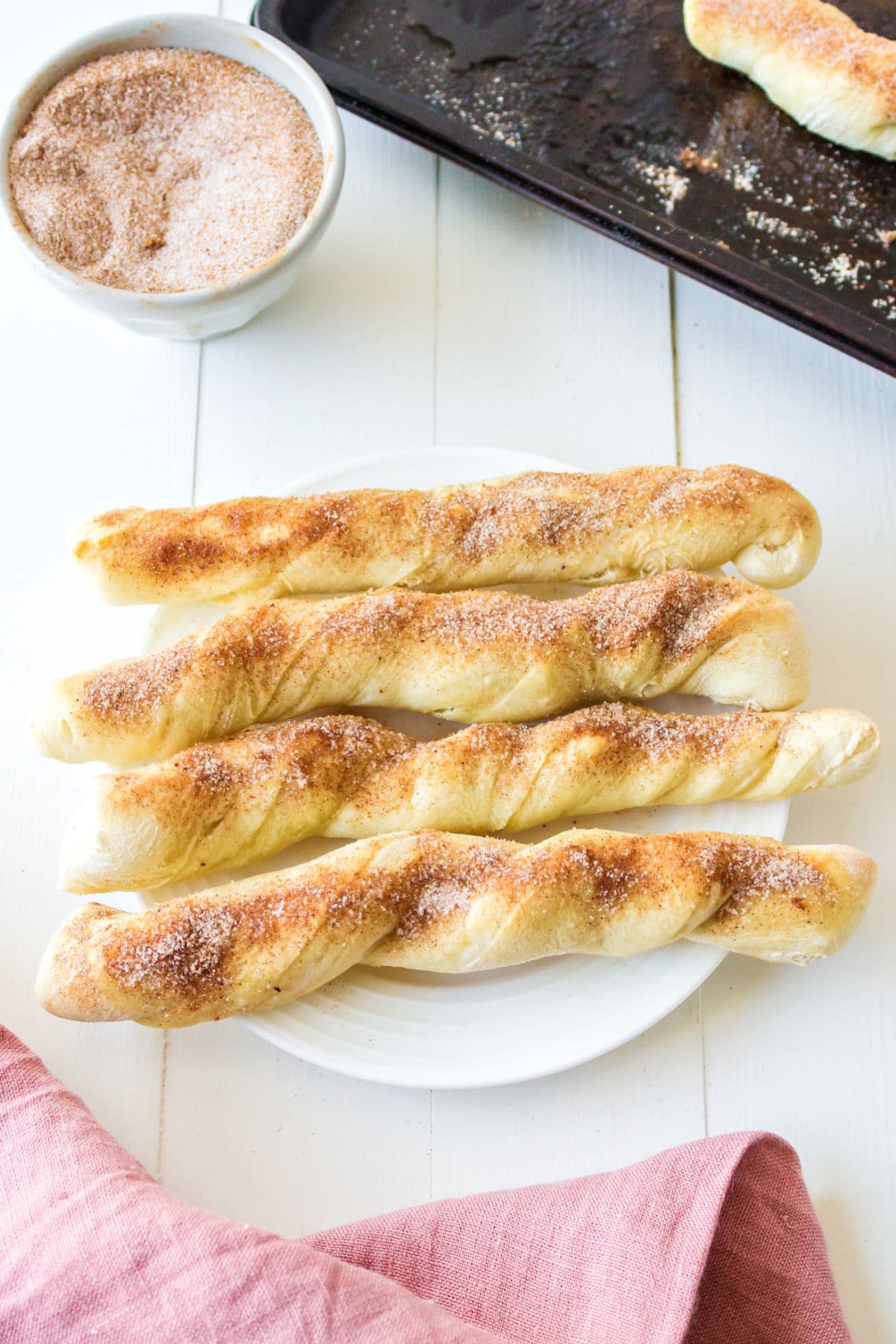 Four cinnamon sugar breadsticks on a white plate.