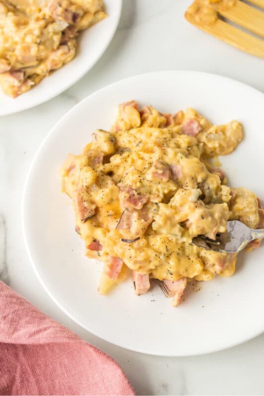 A silver fork taking a bite of scalloped potatoes with ham.