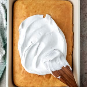 A wooden spatula spreading seven minute frosting onto a yellow cake.