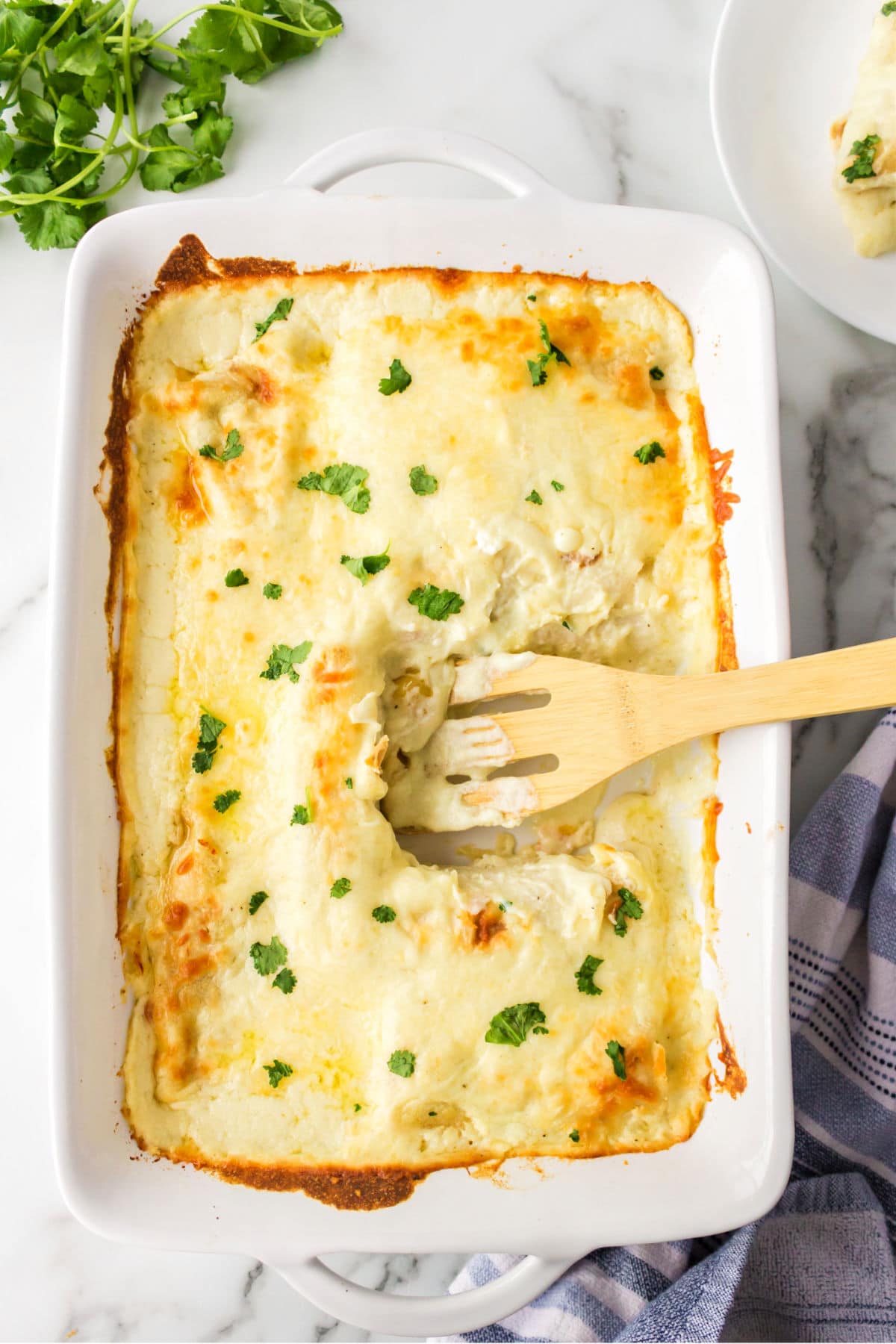 A wooden turner removing enchiladas from a pan.