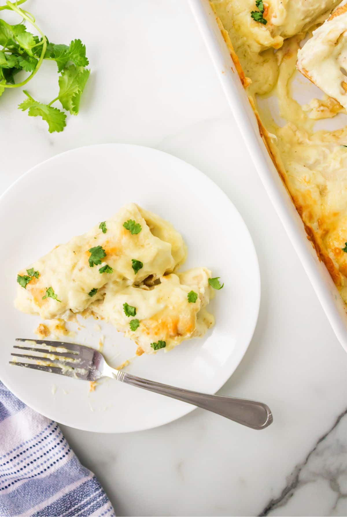 A white chicken enchilada and a half enchilada on a white plate. 