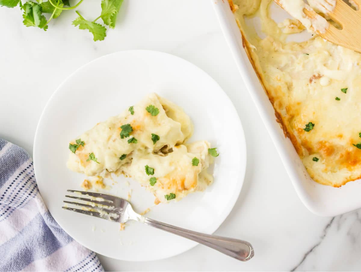 A plate with two white chicken enchiladas on it with a bite missing.