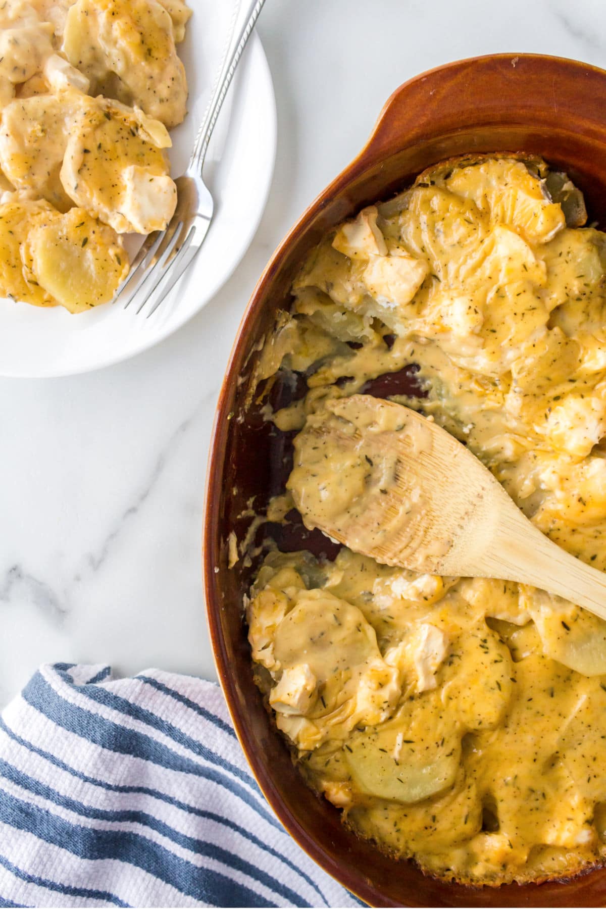 Dish of cream cheese scalloped potatoes with a wooden spoon in it. 