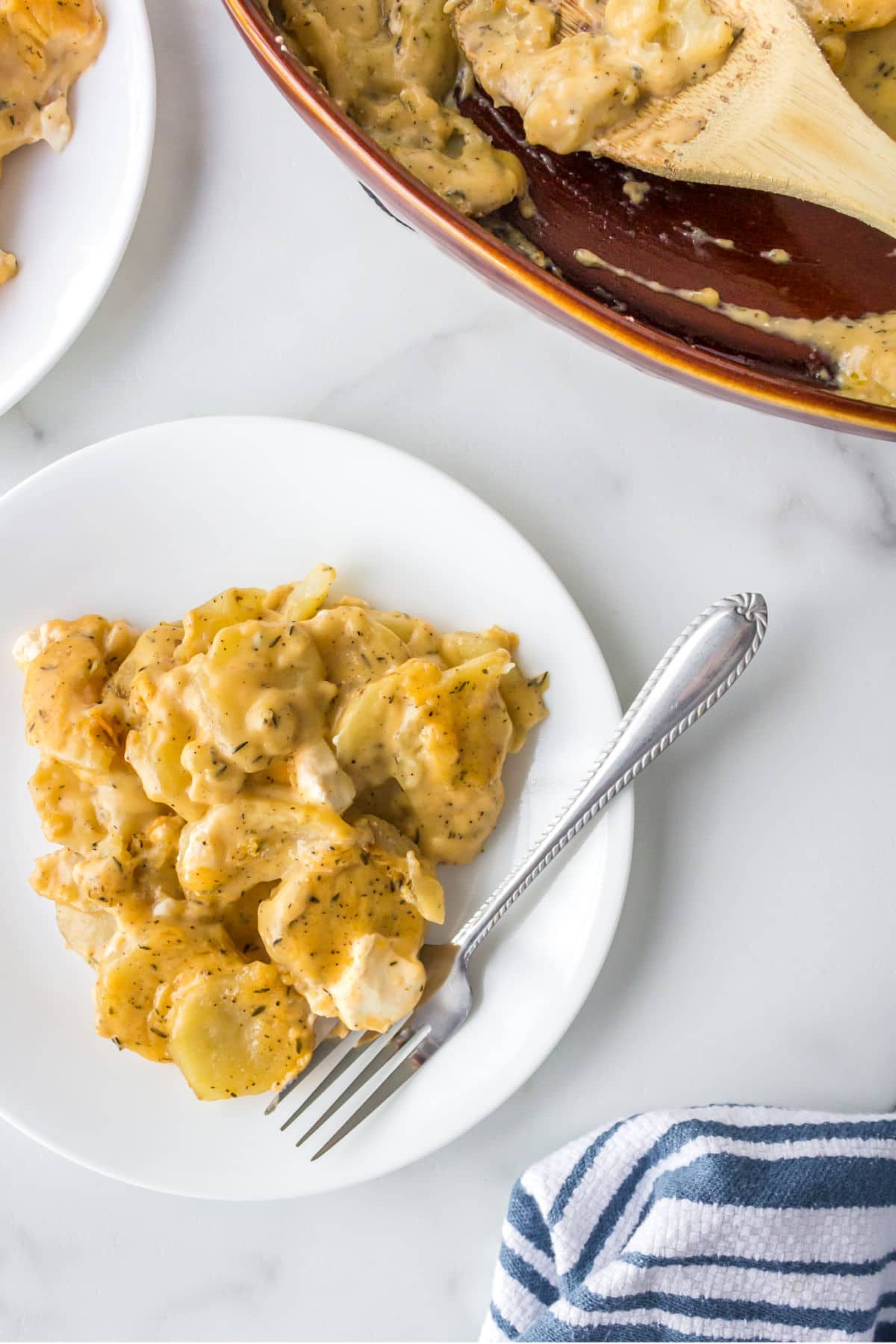 White plate of cream cheese scalloped potatoes with a silver fork in it. 