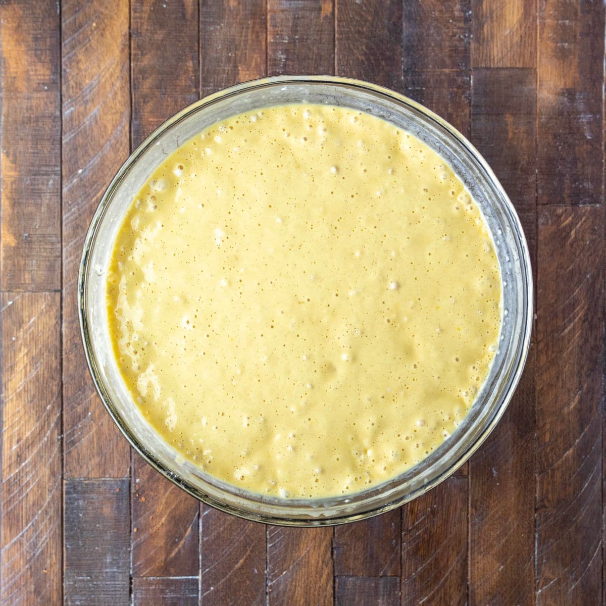 Glass mixing bowl with yeast waffle batter that has rested.