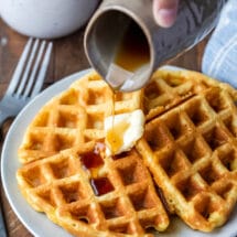 Pitcher pouring maple syrup into a plate of waffles.