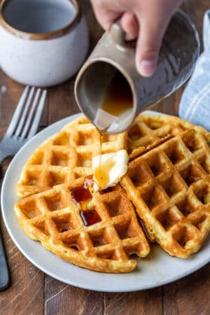 Pitcher pouring maple syrup into a plate of waffles.