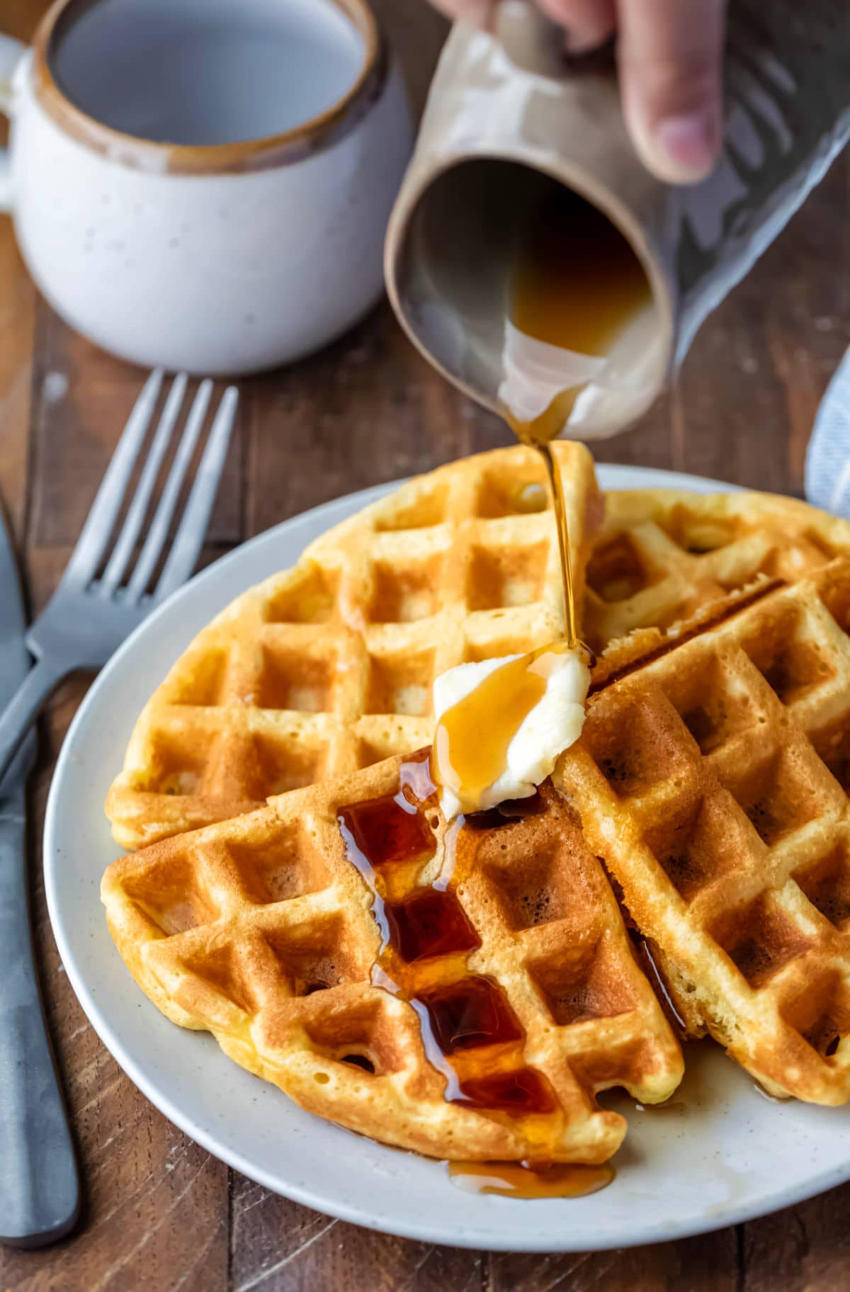 Syrup pouring onto a pat of butter on four waffles.