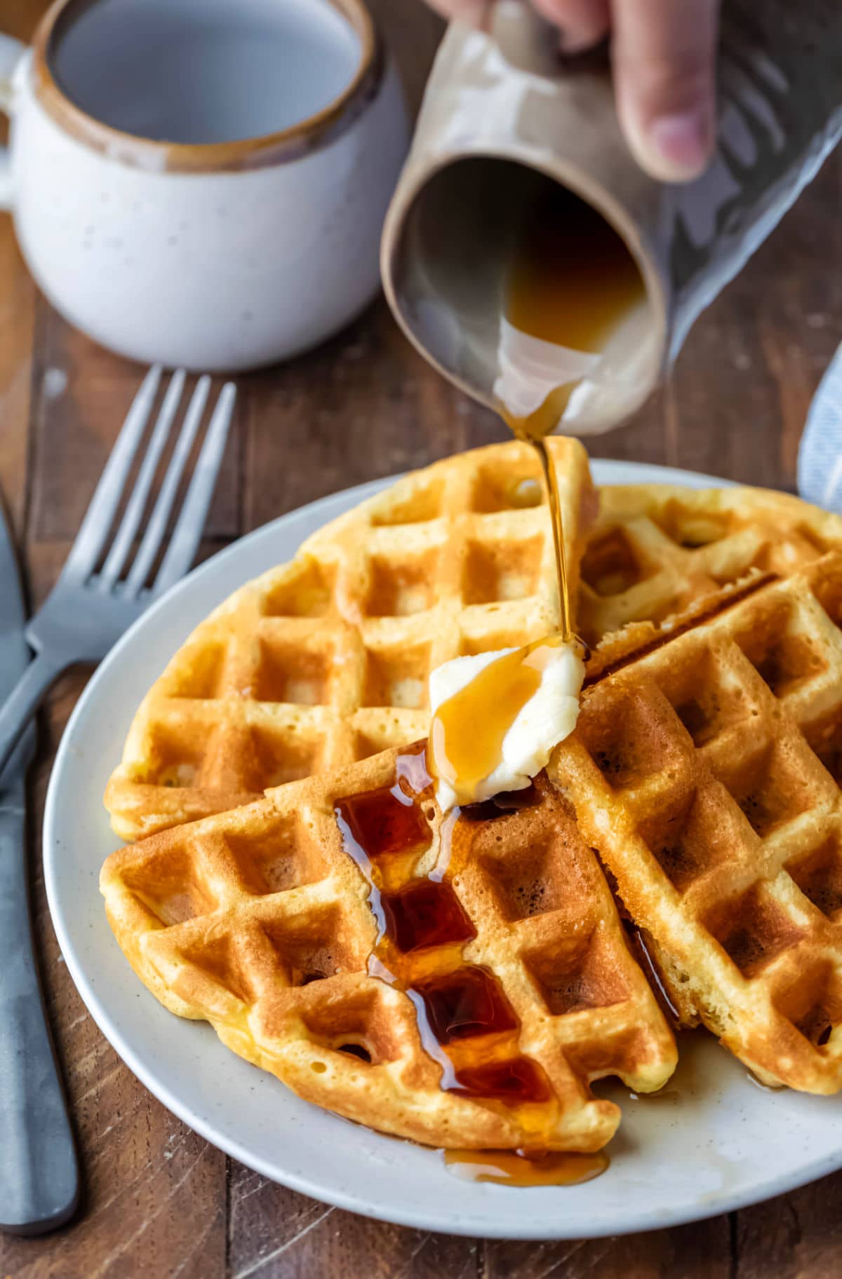 Syrup pouring onto a pat of butter on four waffles. 