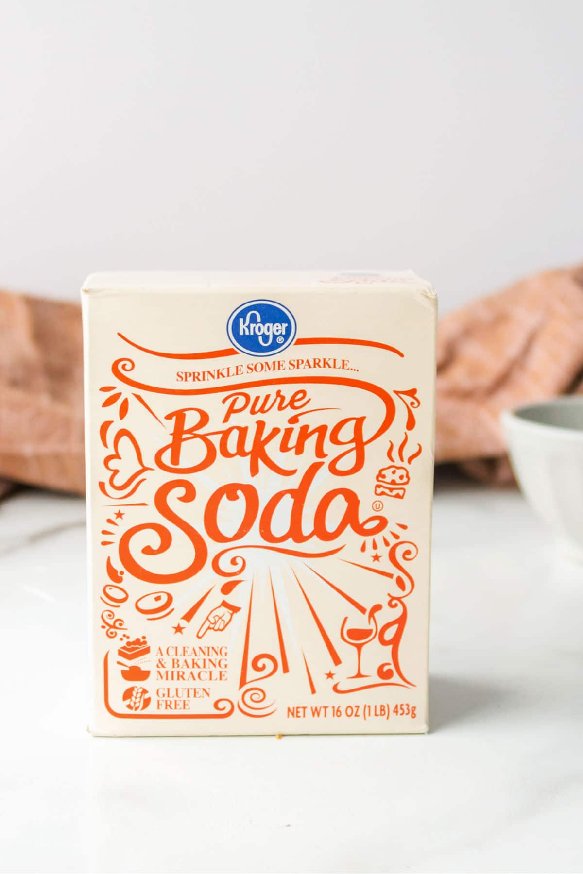 A box of baking soda next to a white bowl. 