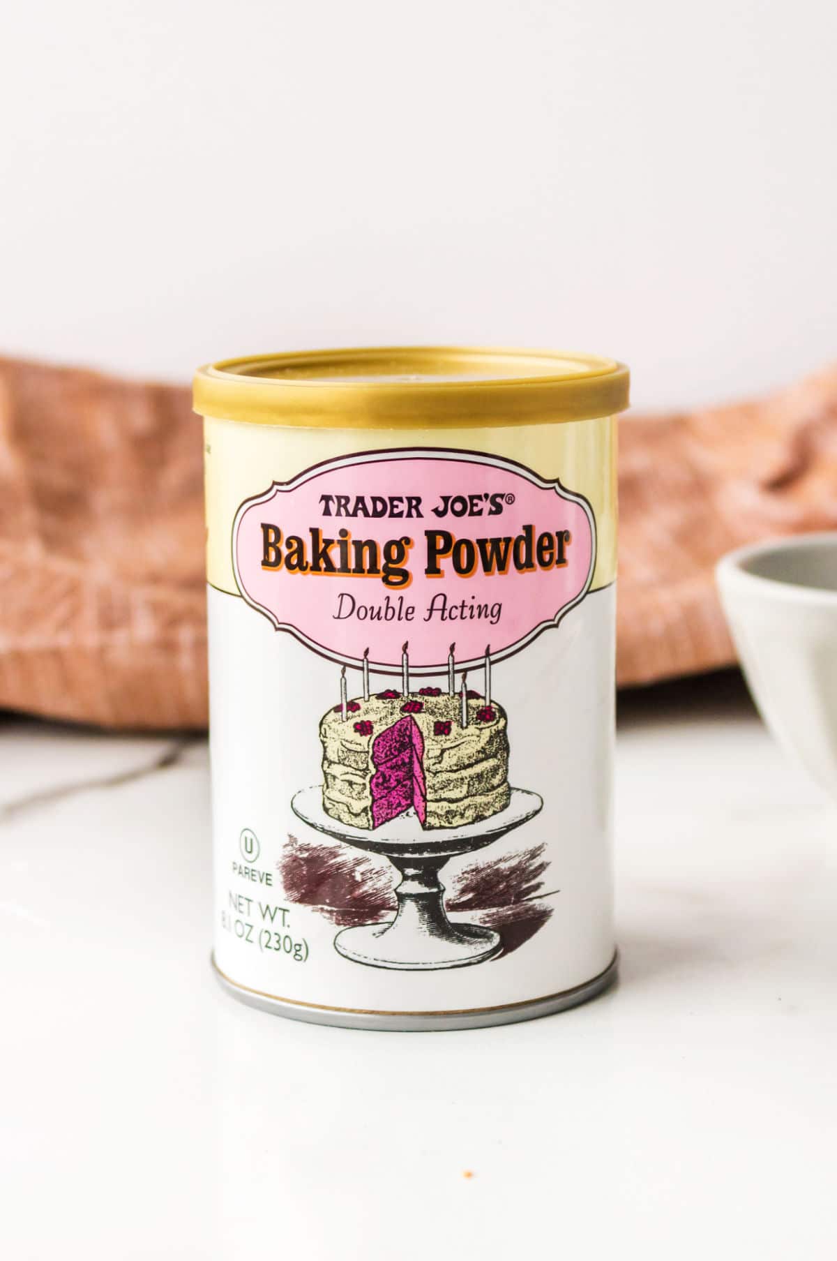Can of baking powder next to a white bowl.