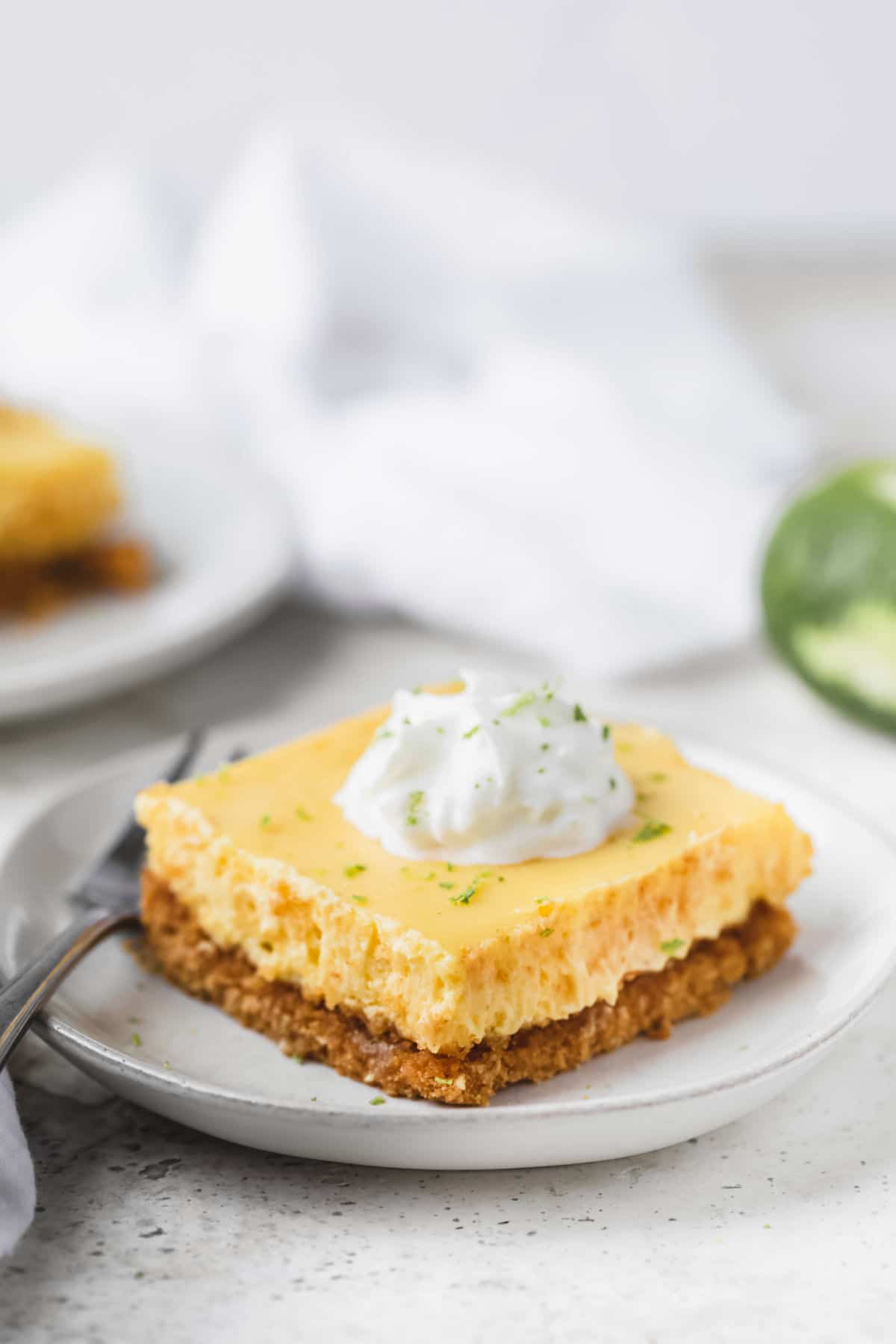 Key lime pie bar next to a partially zested lime. 